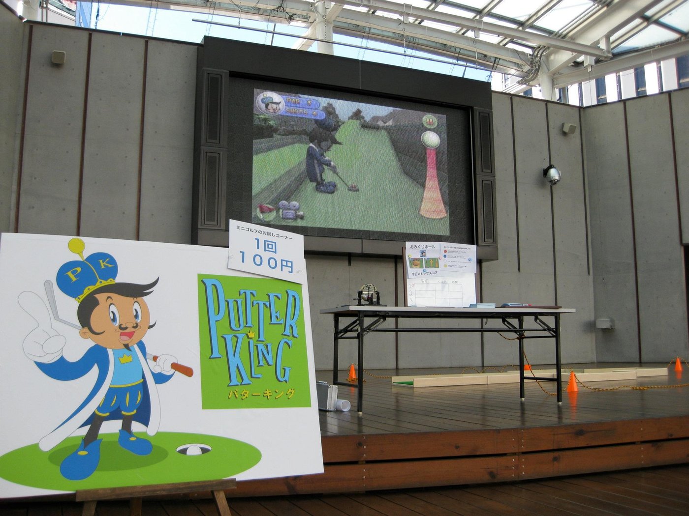 A wide shot of the Putter King app demo booth with a large screen, easel poster, and mini-golf setup