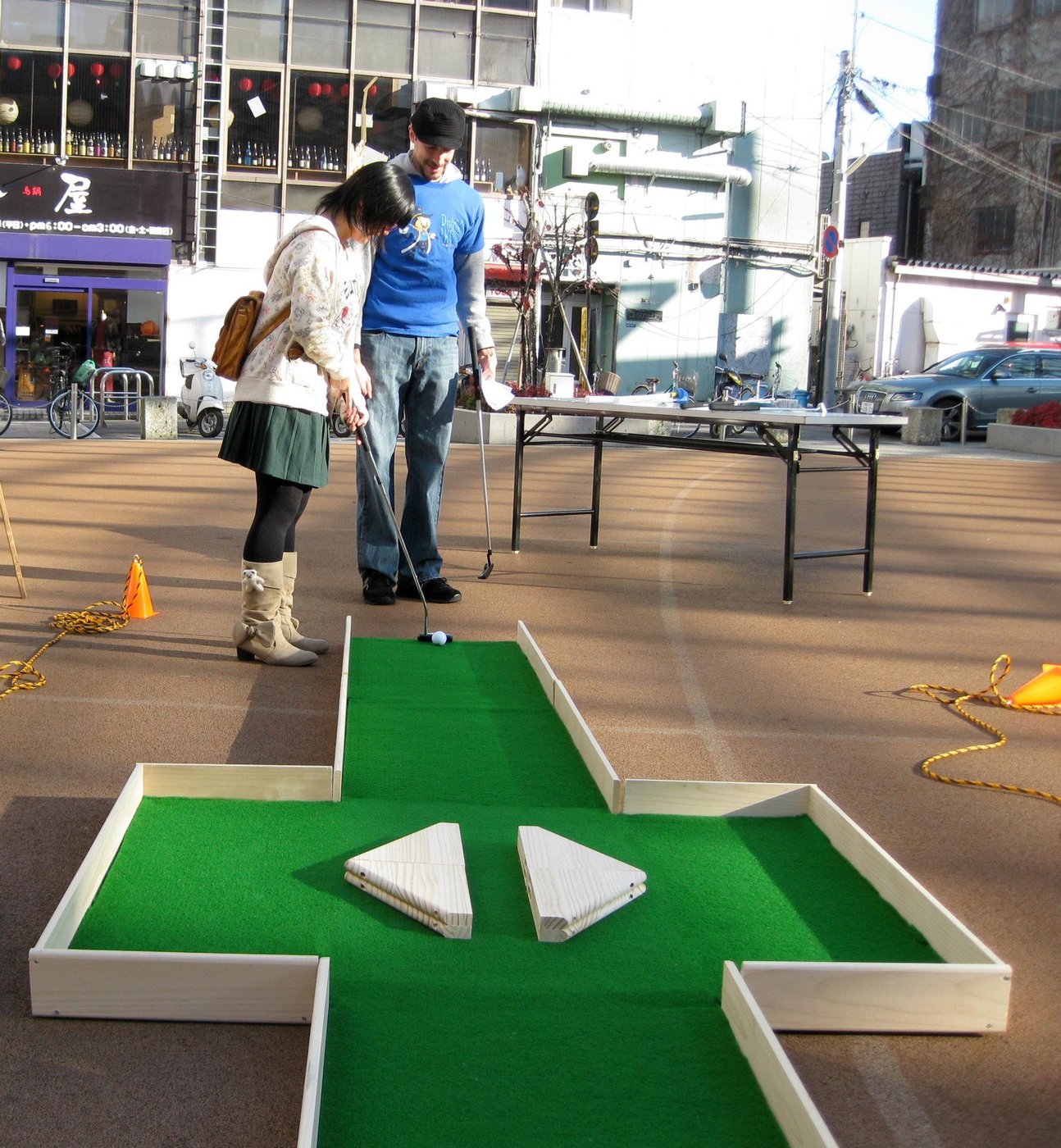 A couple lining up a putt on a pop-up miniature-golf hole in the middle of a Japanese street