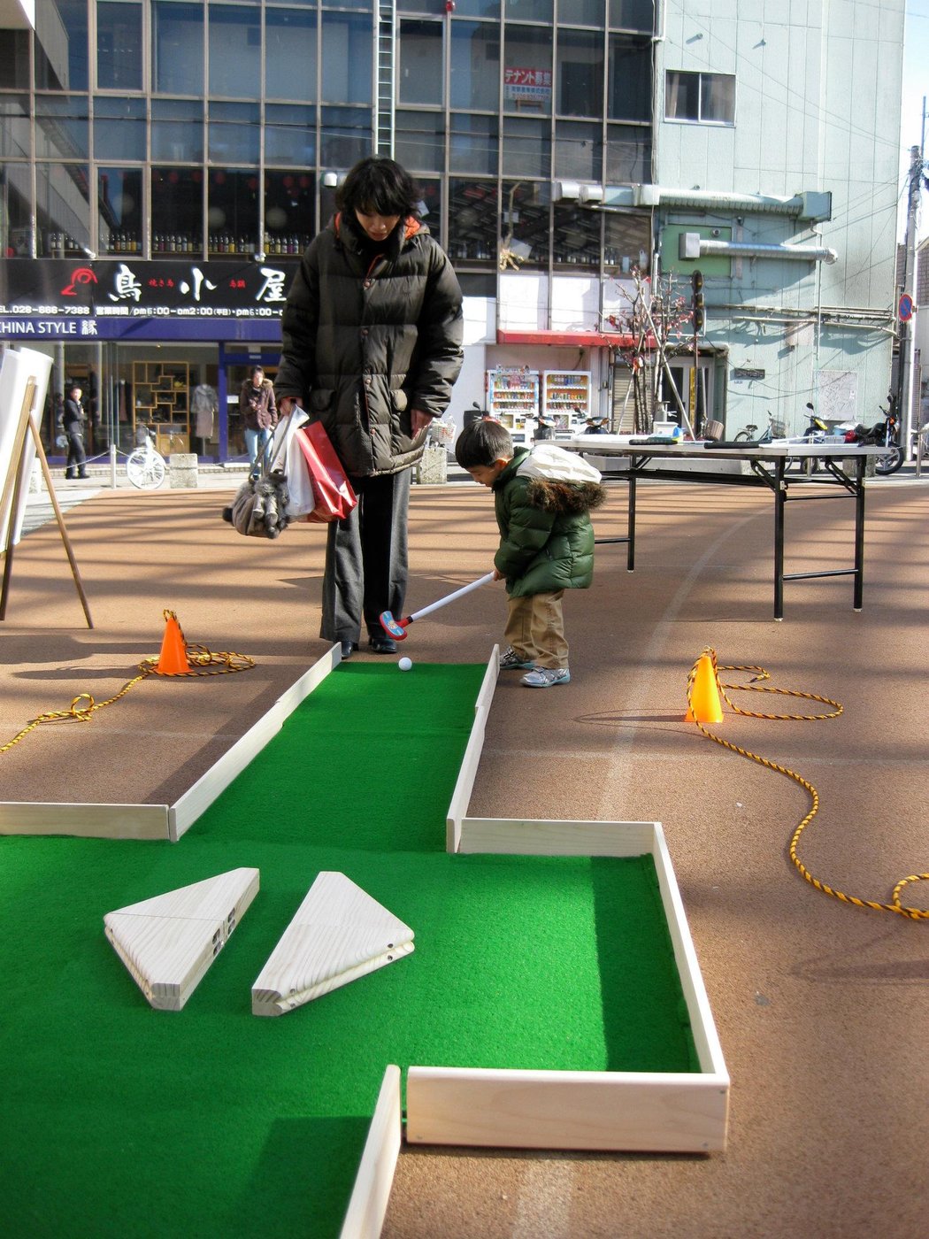 A mother and small child playing on the pop-up mini-golf hole on a Japanese shopping street